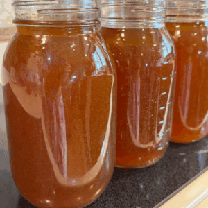 Mason jars filled with rich, homemade beef bone broth lined up on a stove