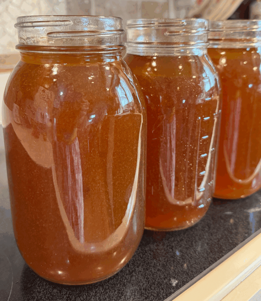 Mason jars filled with rich, homemade beef bone broth lined up on a stove