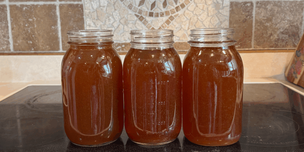 Three quart jars of homemade beef bone broth cooling on the stove