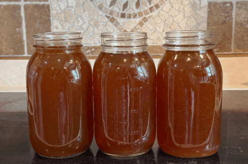 Three quart jars of homemade beef bone broth cooling on the stove