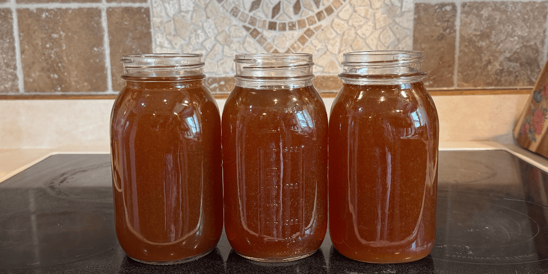 Three quart jars of homemade beef bone broth cooling on the stove