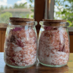 Glass jars with cork lids filled with peony bath soak on a rustic table
