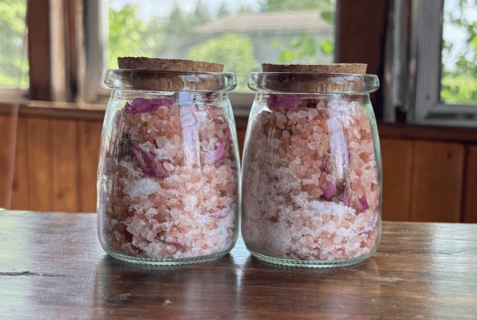 Glass jars with cork lids filled with peony bath soak on a rustic table