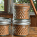 3 jars of homemade apple pie spice with a cinnamon stick leaning against them
