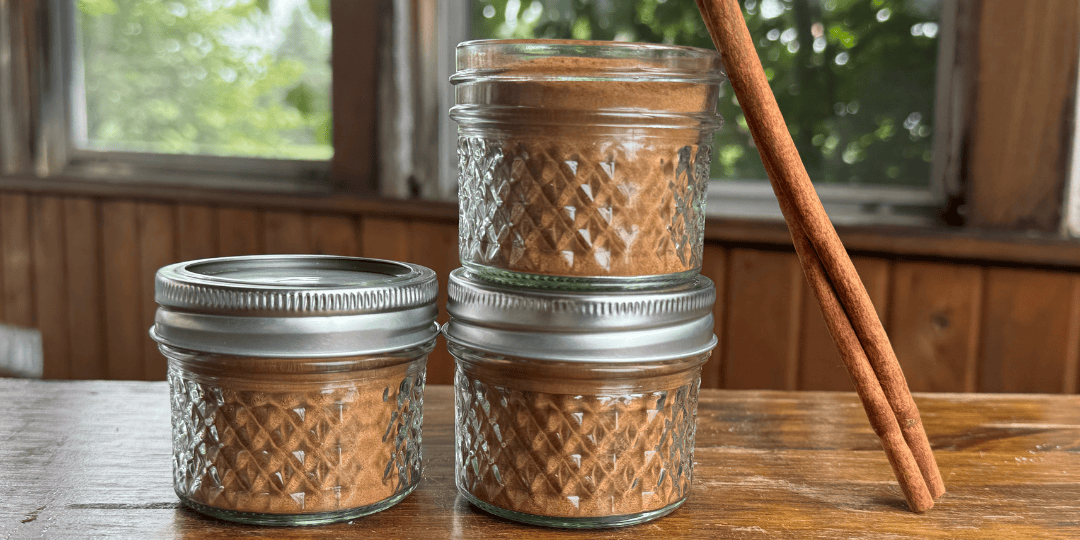 3 jars of homemade apple pie spice with a cinnamon stick leaning against them