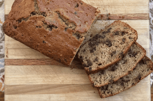 sliced chocolate chip zucchini bread on a wood cutting board, kitchen towel, and wooden table