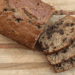 sliced chocolate chip zucchini bread on a wood cutting board, kitchen towel, and wooden table