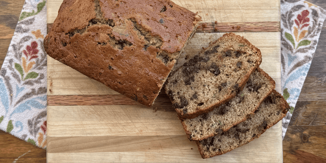 sliced chocolate chip zucchini bread on a wood cutting board, kitchen towel, and wooden table