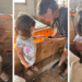 Toddler and older child gently holding and kissing baby chicks near a DIY wooden brooder on a homestead