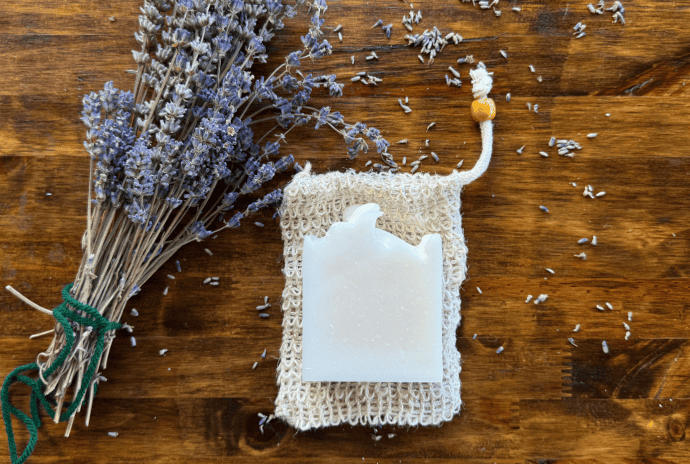 Lavender tallow soap bar placed on a soap saver bag next to a dried lavender bundle