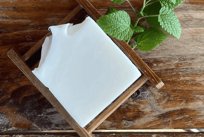 Natural tallow soap on a bamboo tray with fresh peppermint leaves beside it