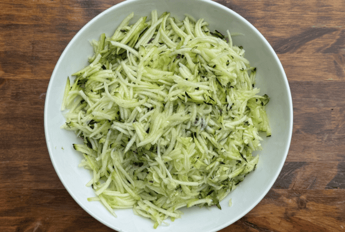 shredded zucchini in a white bowl on a wooden table