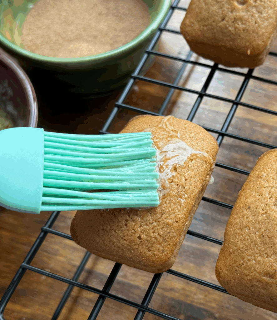 brushing butter on homemade apple cider donut mini bread loaves on a cooling rack