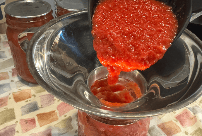 ladling freshly made tomato sauce into pint sized jars to can