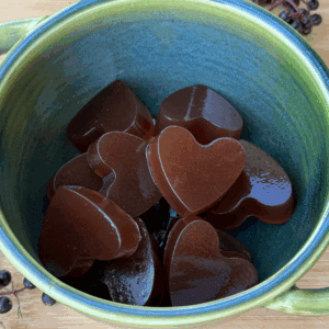 heart shaped elderberry gummies in a bowl with fresh elderberries next to it.